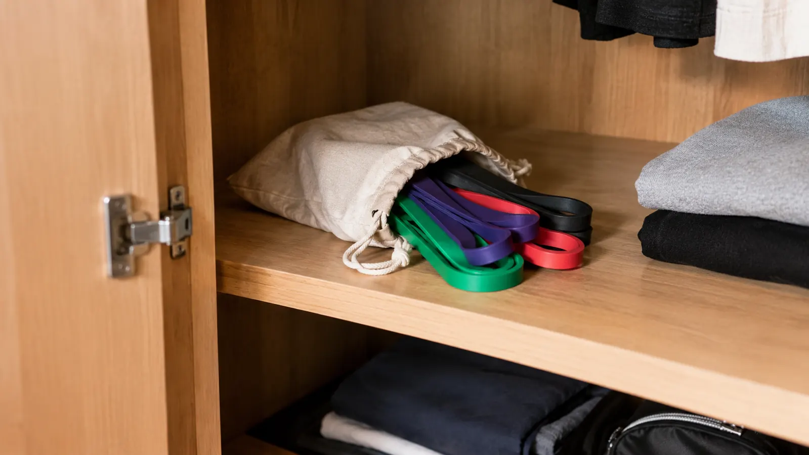 A small cloth drawstring bag with resistance bands stored on a closet shelf, the closet door open.